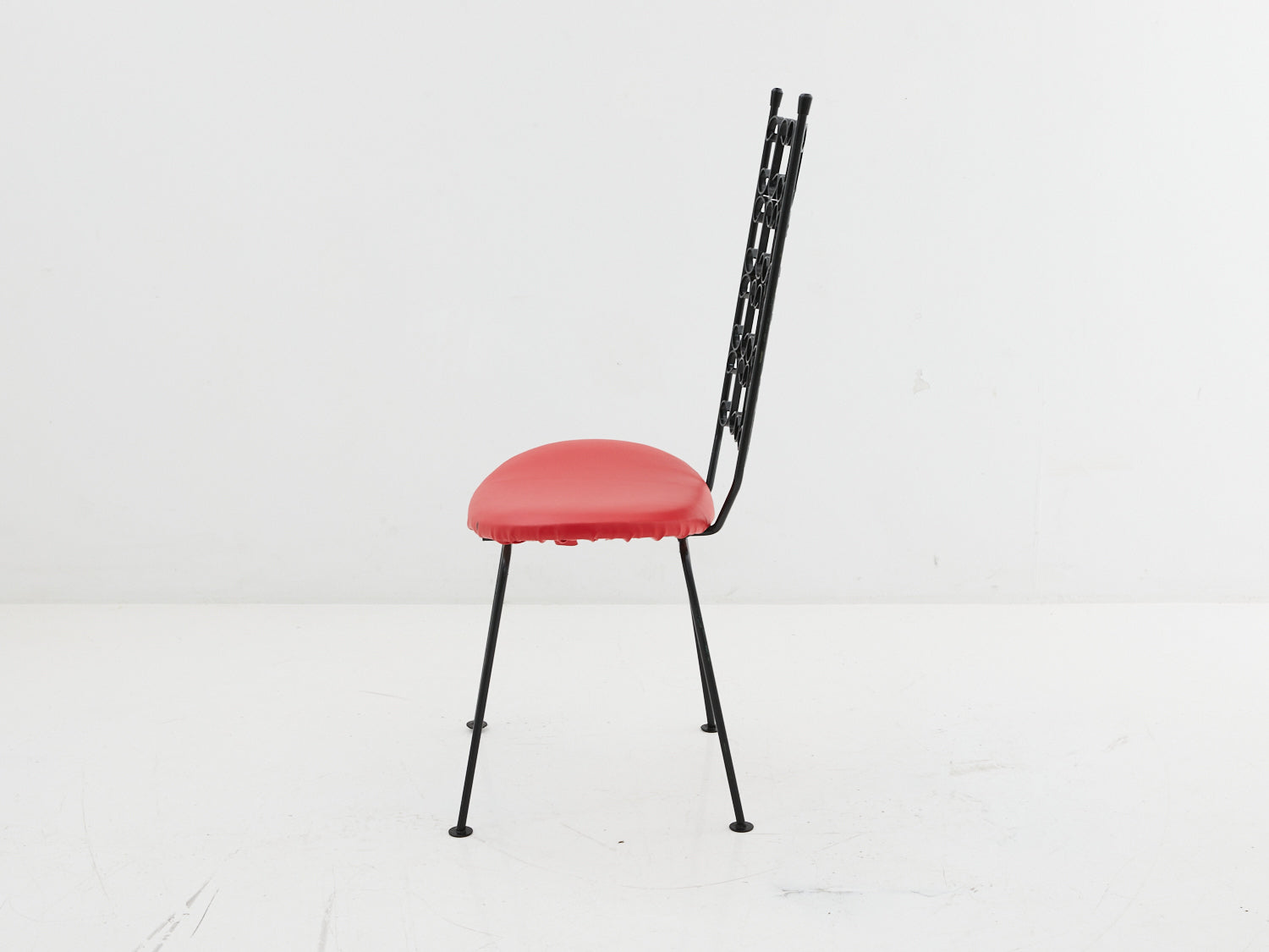 Side view of an iron scroll dining chair with red seat cushion designed by Arthur Umanoff circa 1960s