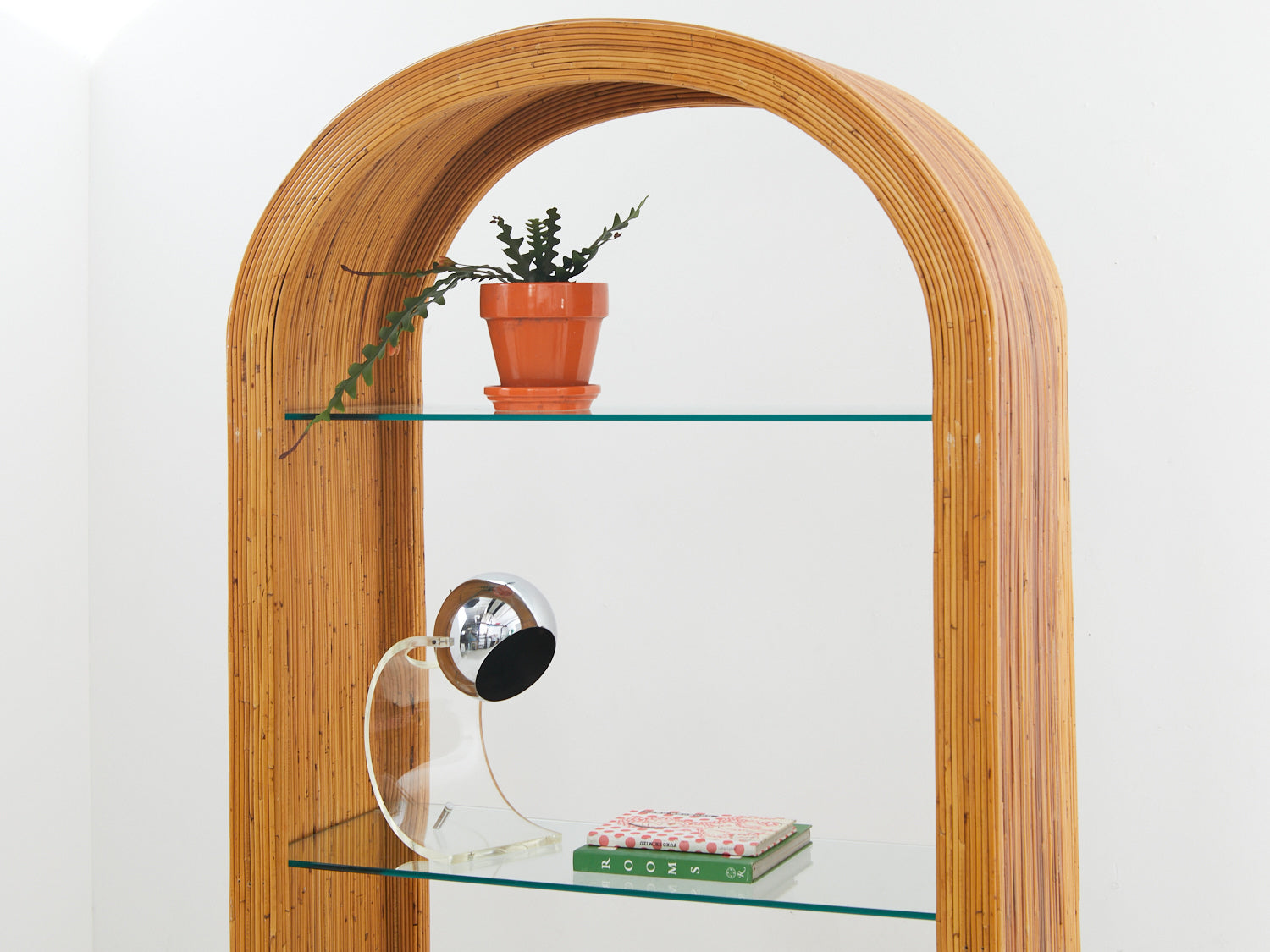 Pencil reed etagere with a plant, lamp, and books on the glass shelves