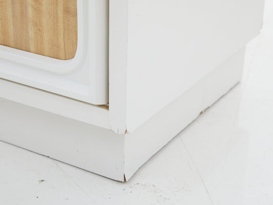 Close up of damage to the wood on a white dresser with faux wood