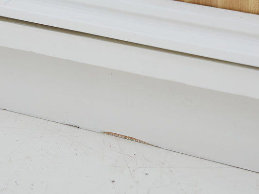close up of damage to the base of a white dresser with faux wood formica details