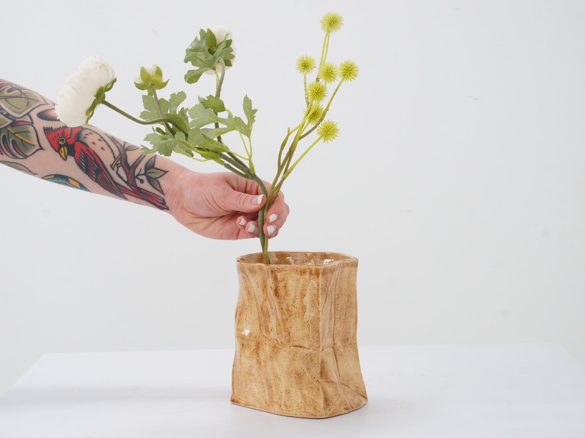 Ceramic paper bag vase with hand and flowers reaching in from left